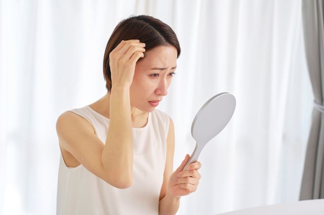鏡で髪の毛を見て悩む40代の女性